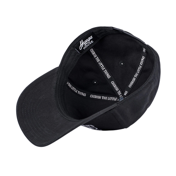 Flat lay of Huega House Circuit Hat in Black highlighting the tonal front logo, flat brim, and performance-inspired construction