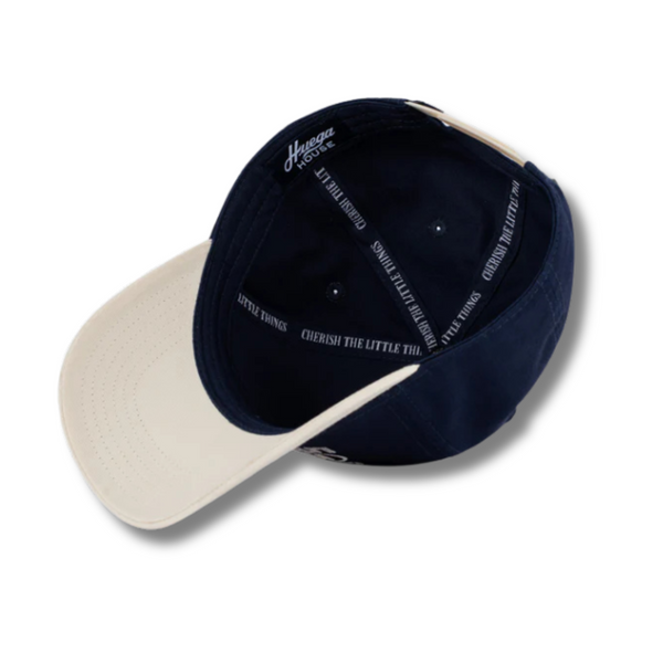 Flat lay of Huega House Circuit Hat in Natural/Navy highlighting clean embroidered logo, flat navy brim, and structured front panel