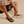 Person wearing OluKai Ulele sandals in black during a casual, beachside walk