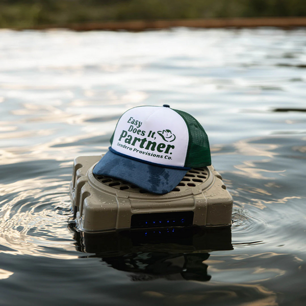 Person wearing the Sendero Easy Does It Hat in White and Green in a laid-back, sunny outdoor setting